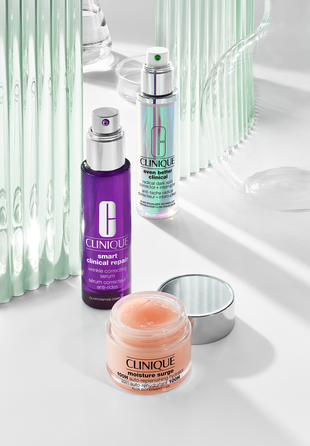 Three Clinique skincare products displayed: a purple wrinkle serum, a silver corrective serum, and a peach moisturizing cream on a sleek surface.