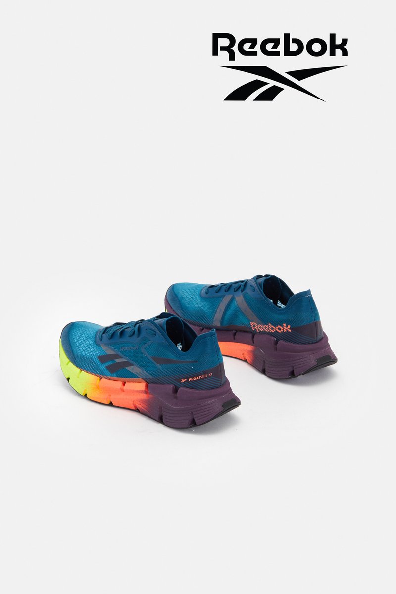 Blaue Reebok-Laufschuhe mit einer mehrfarbigen Sohle, die einen Farbverlauf von Gelb zu Orange zeigt, vor einem weißen Hintergrund ausgestellt.