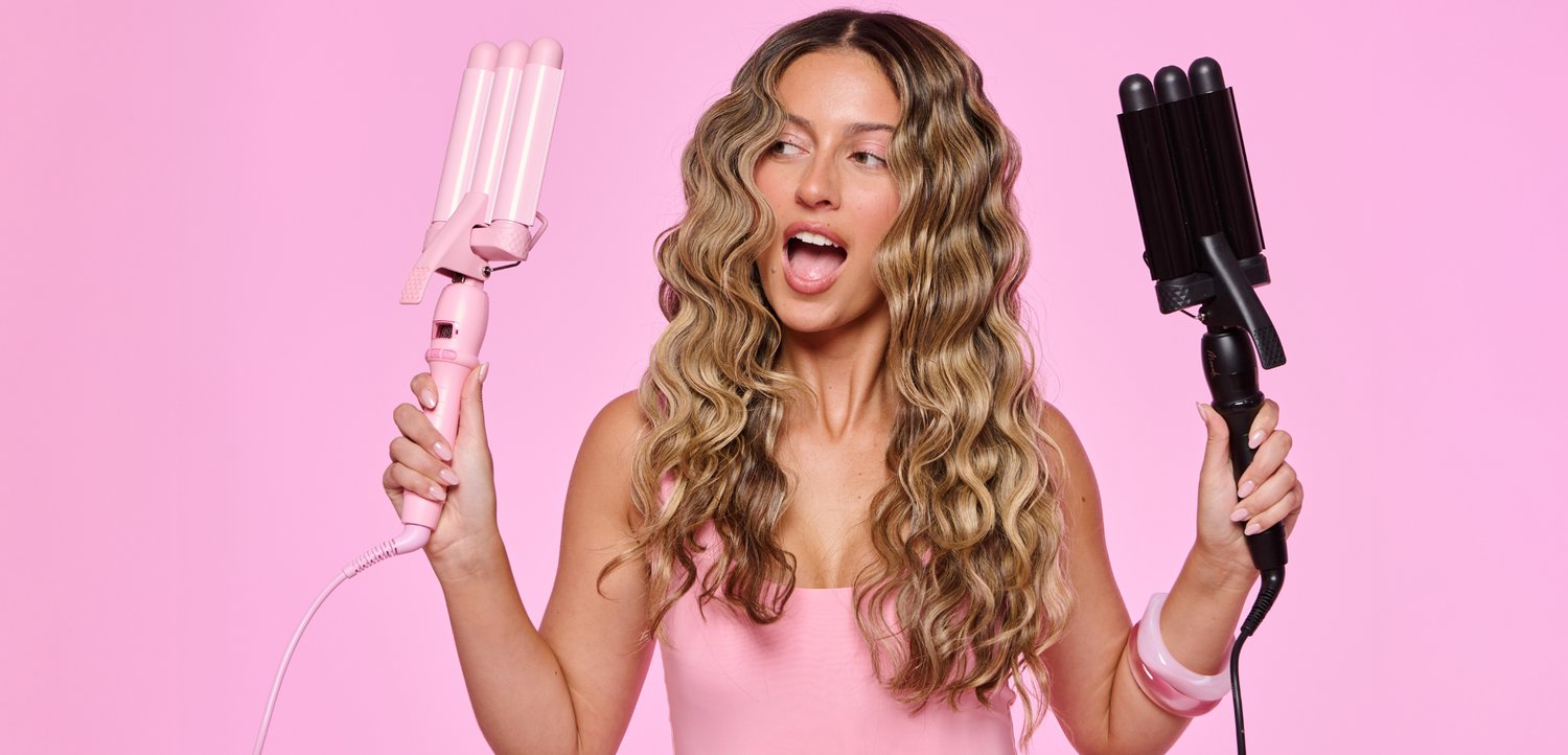 Femme aux longs cheveux ondulés tient deux bigoudis triples, un rose et un noir, sur un fond rose uni.
