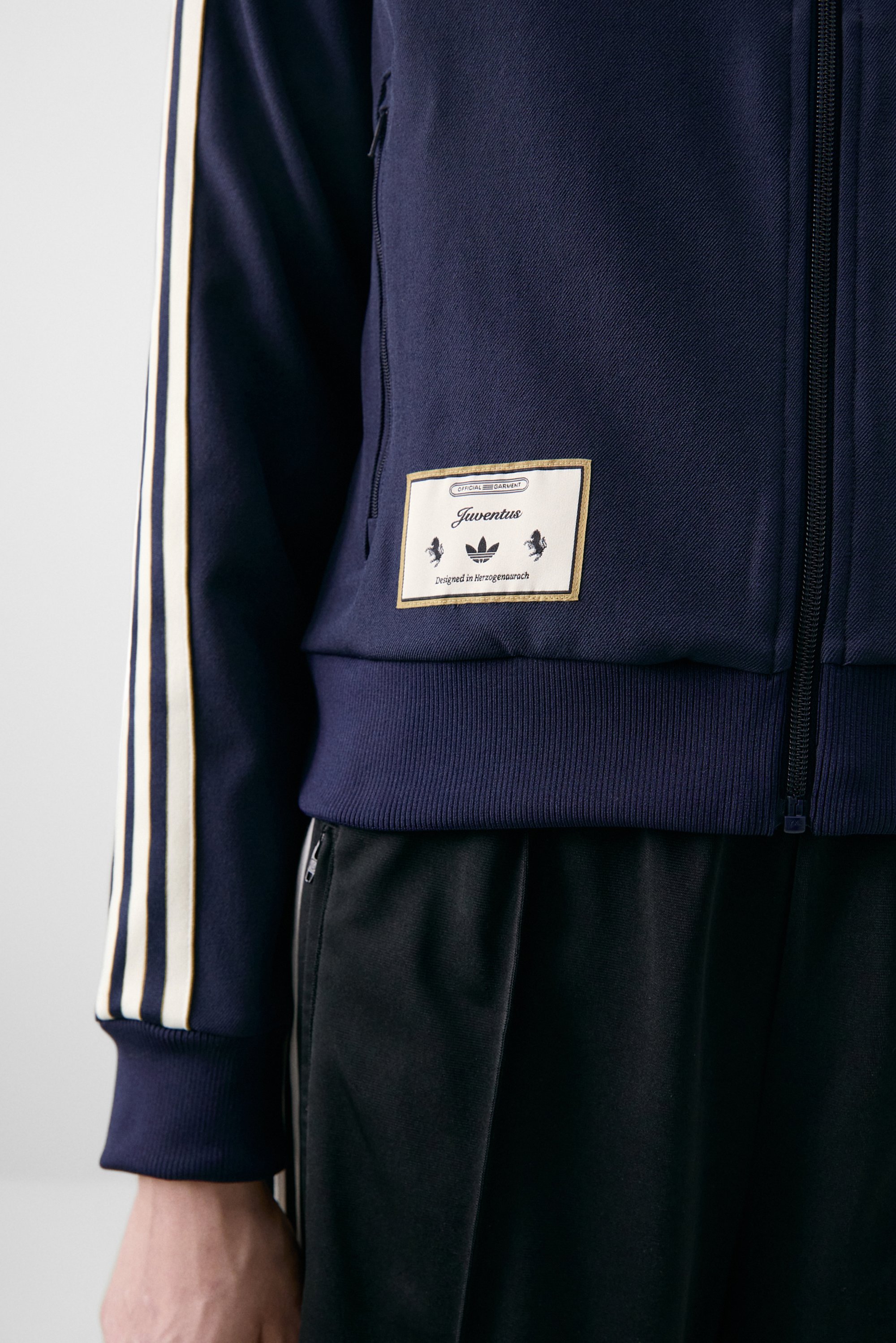Marineblauwe sportjack met witte strepen, met een "Juventus" label en zwarte broek, die een sportieve stijl weergeeft.
