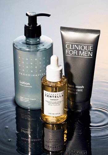 Three skincare products on a reflective wet surface: Skandinavisk lotion with pump, SKIN1004 Centella ampoule, and Clinique for Men face wash.