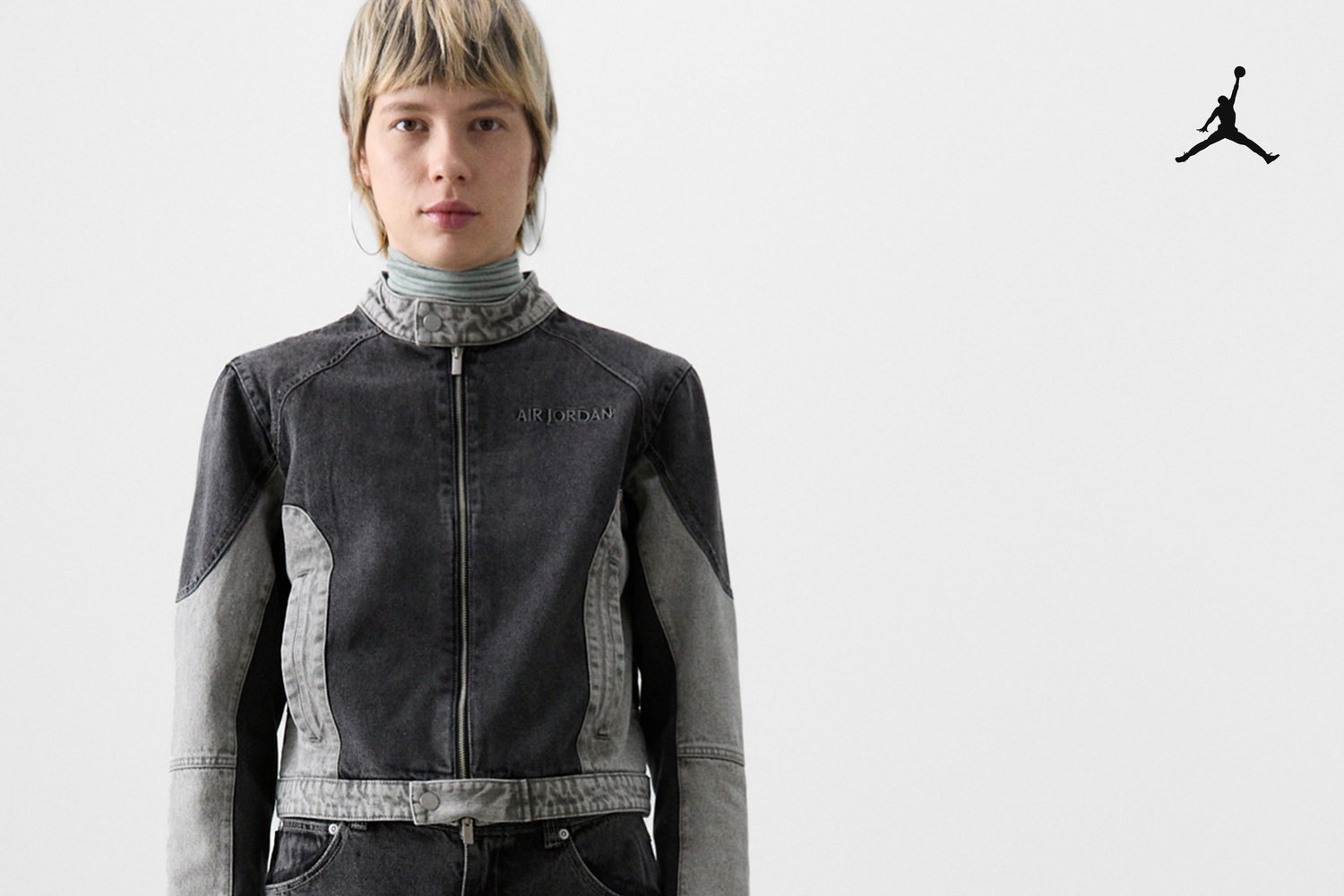 Model wearing a black and grey denim jacket with "Air Jordan" logo, stands against a plain white background, showcasing a contemporary style.