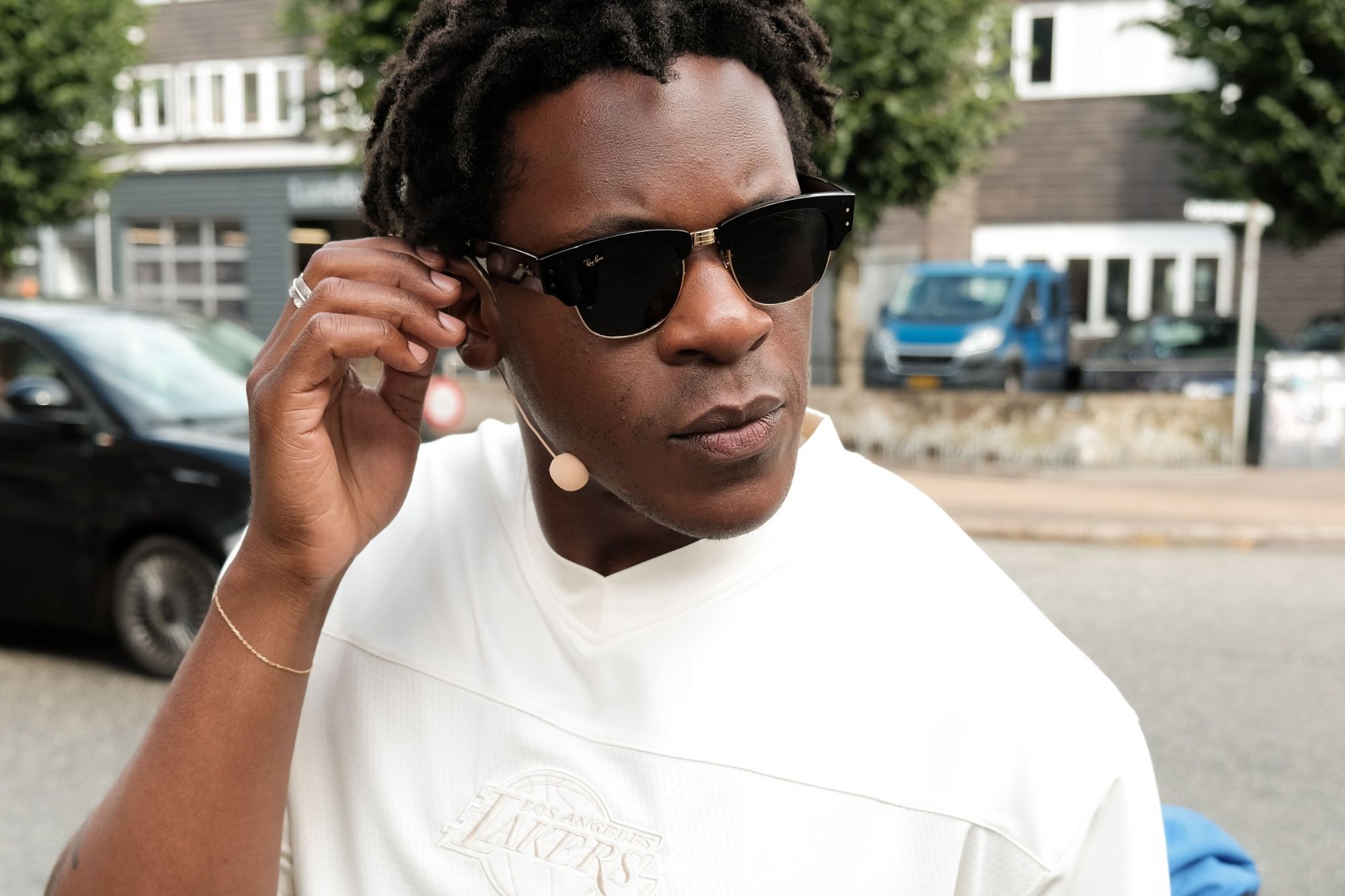 Schwarze Sonnenbrille mit dickem Schildpattmuster, goldenen Akzenten und einem beigefarbenen Mikrofon angebracht. Das Subjekt trägt einen weißen Pullover.
