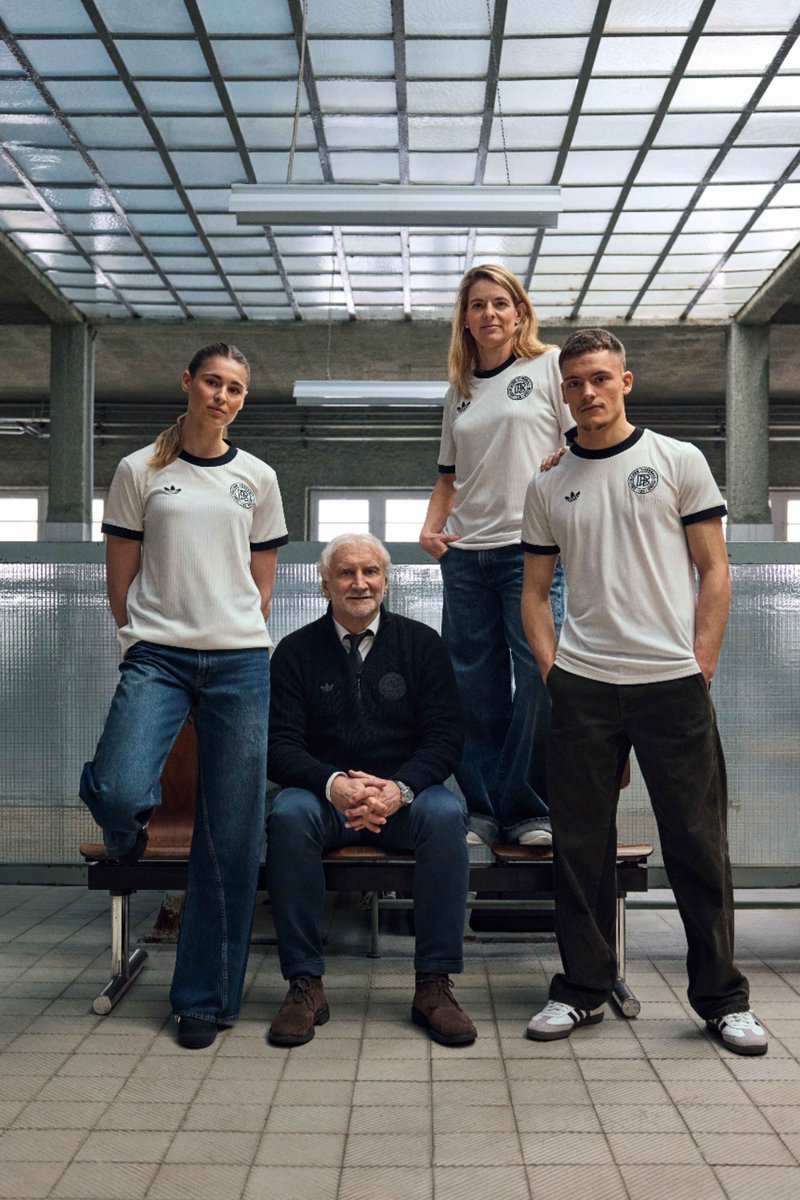 Four individuals pose in a minimalistic setting, wearing white shirts with black accents. A man sits in front, flanked by three standing figures.