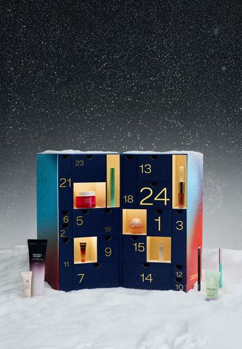 Un calendrier de l’Avent beauté numéroté, avec des tiroirs ouverts laissant voir des cosmétiques, entouré de produits de soin et de maquillage posés sur la neige, sous une chute de neige.