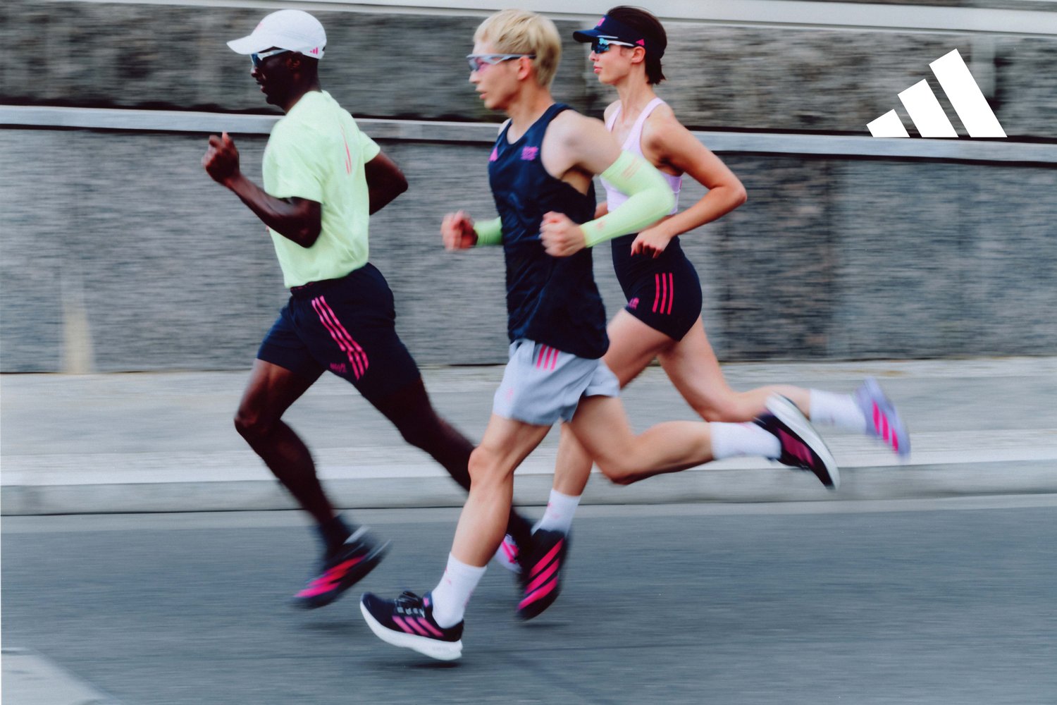Three runners in motion on a pavement. They are wearing athletic gear: neon green, dark blue, and pink outfits, complete with sunglasses and running shoes.