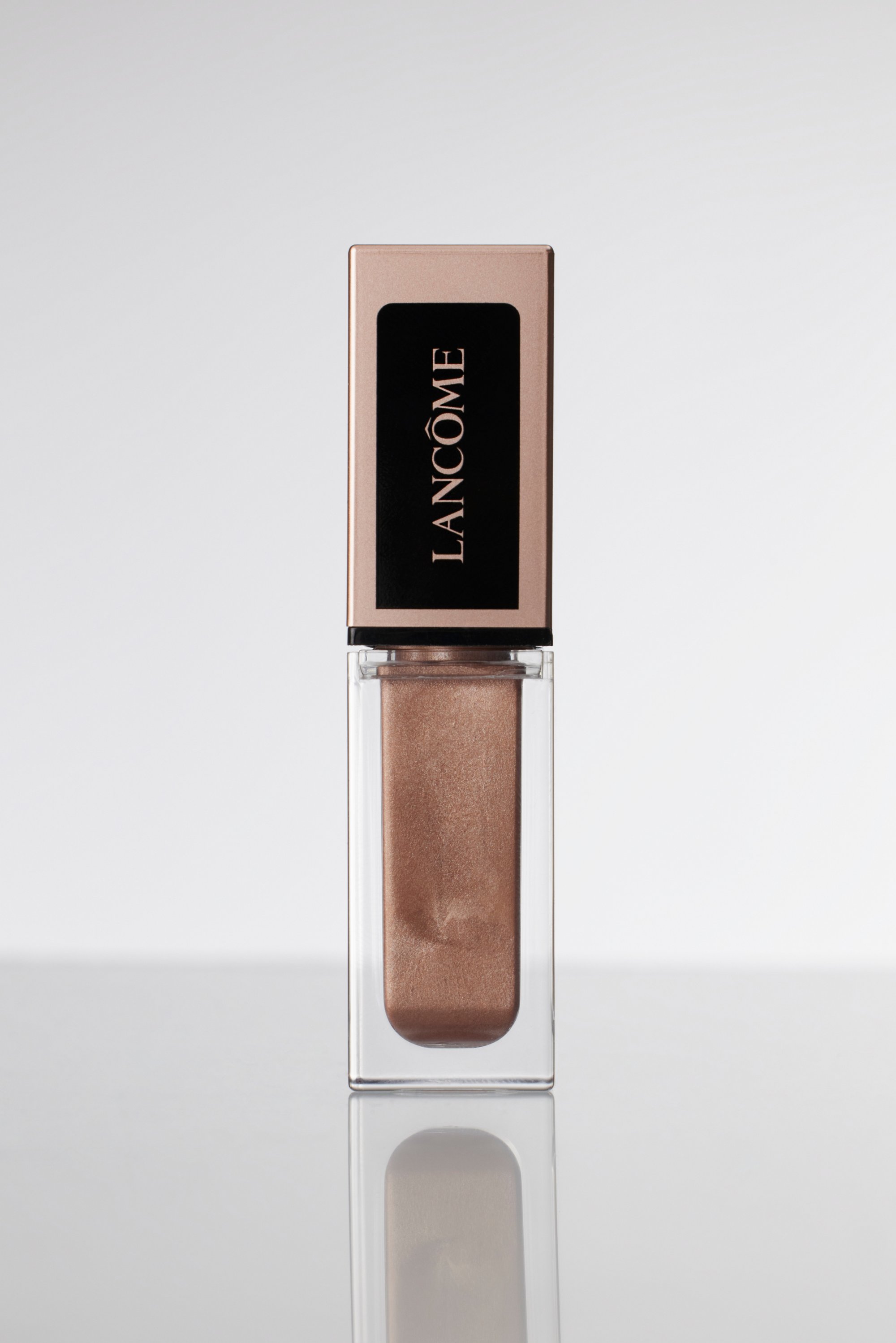 Kiiltoisia huulituotteita läpinäkyvässä astiassa, jossa on metallinhohtoinen pronssinen sävy ja tyylikäs, ruusukultainen korkki, jossa on selkeästi näkyvä "Lancôme"-logo.