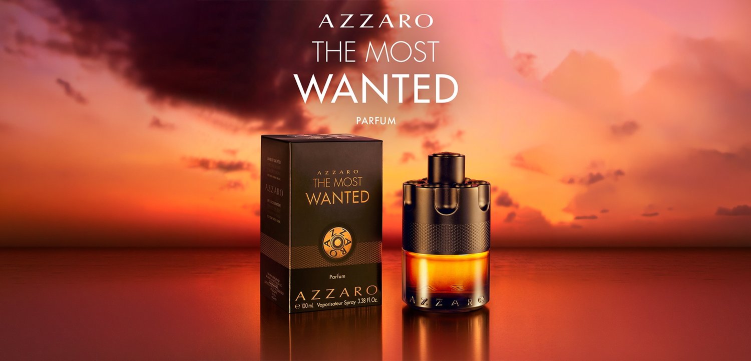 Die Parfümflasche und -verpackung von Azzaro The Most Wanted sind vor einem lebhaften orangefarbenen Sonnenuntergangshimmel mit Wolken zu sehen.
