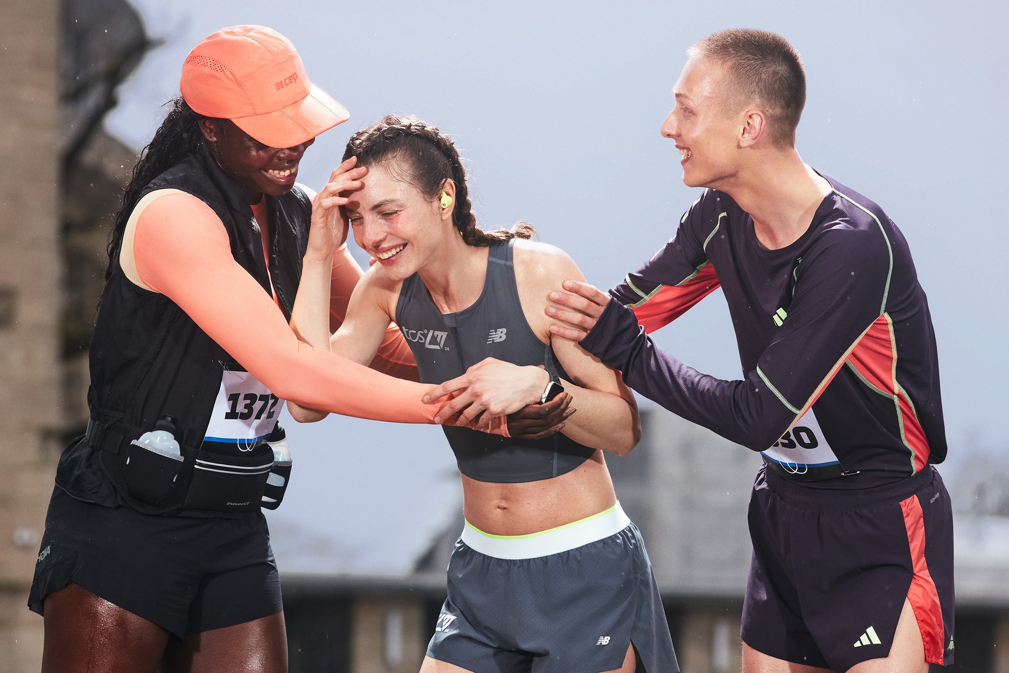 Tres atletas celebran juntos después de una carrera, sonriendo y riendo, mientras uno coloca la mano en la frente de otro en un momento de alegría.