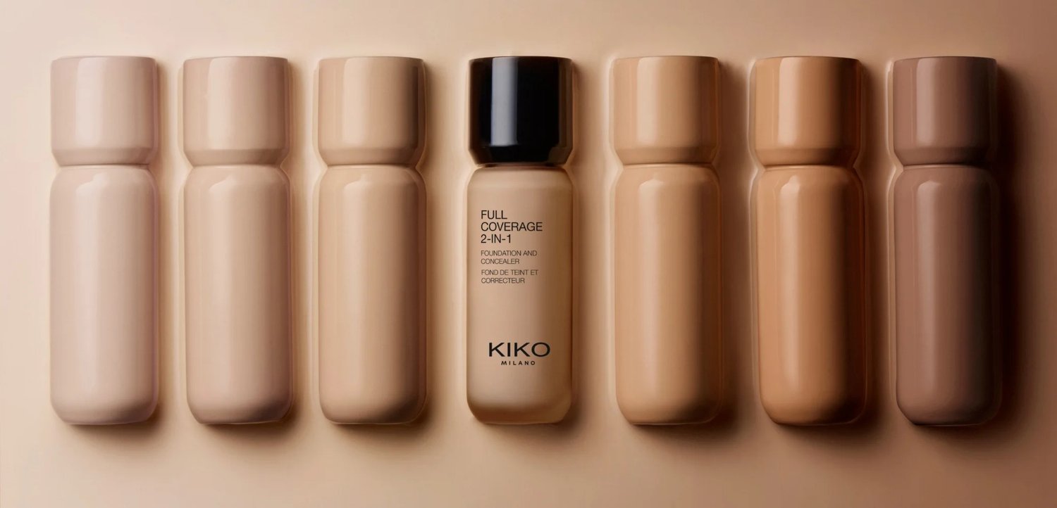 Rangée de sept flacons de fond de teint de nuances variées, dont un étiqueté "KIKO Milano Full Coverage 2-in-1 Foundation and Concealer."