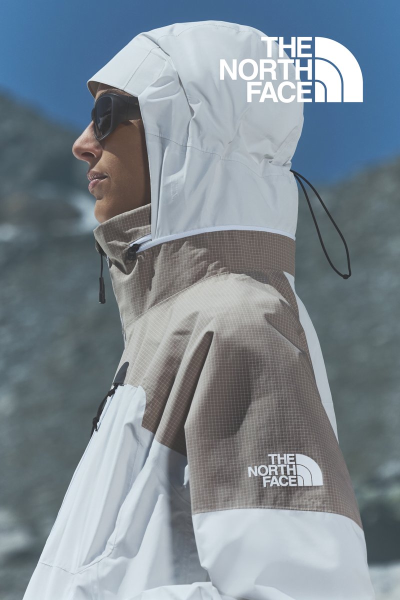 Witte en lichtbruine North Face-jack, met een ruitpatroon, hoge kraag, verstelbare capuchon en logo op de borst.