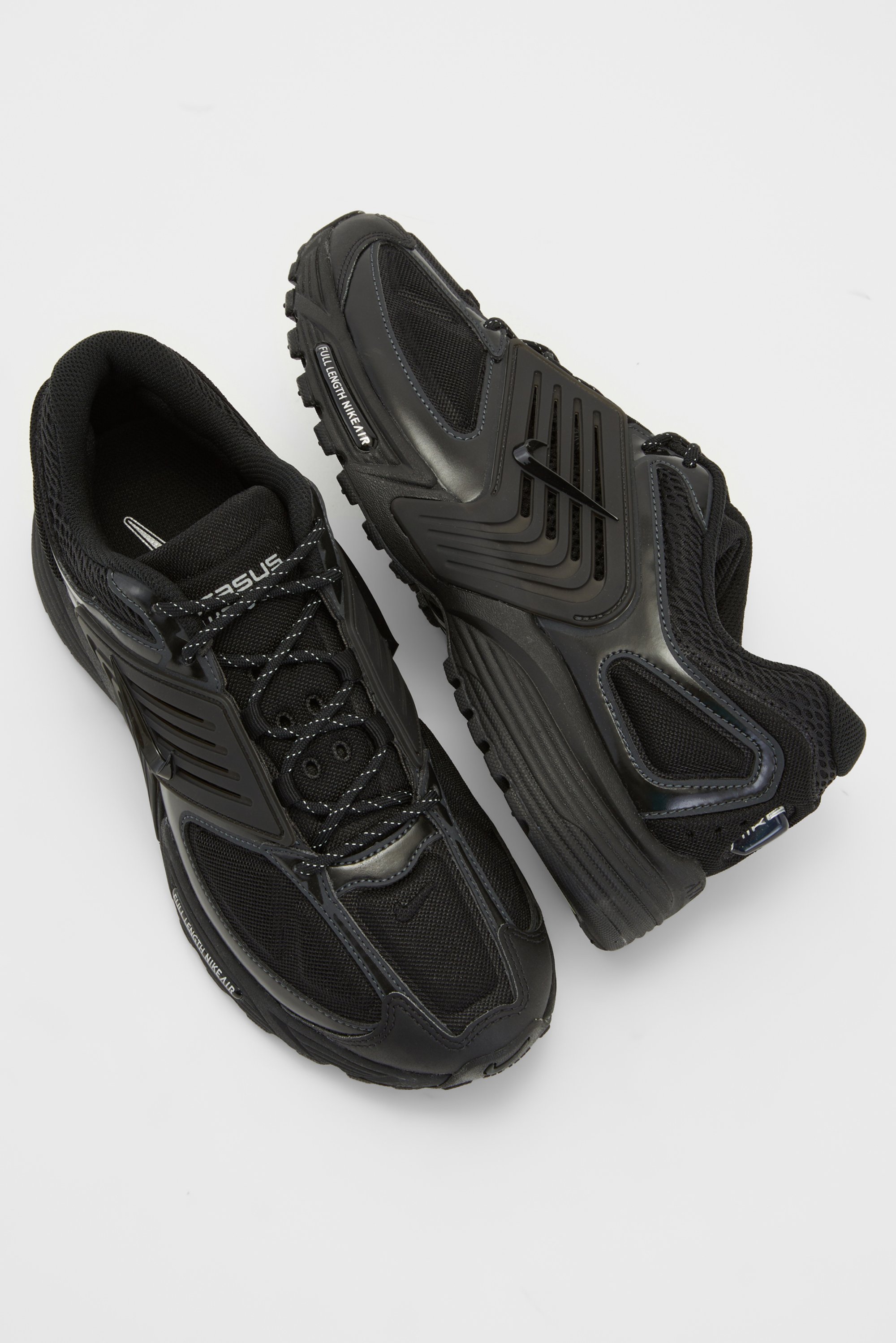 Twee zwarte sportieve schoenen met gaassecties en textuurzolen, naast elkaar geplaatst tegen een eenvoudige witte achtergrond.
