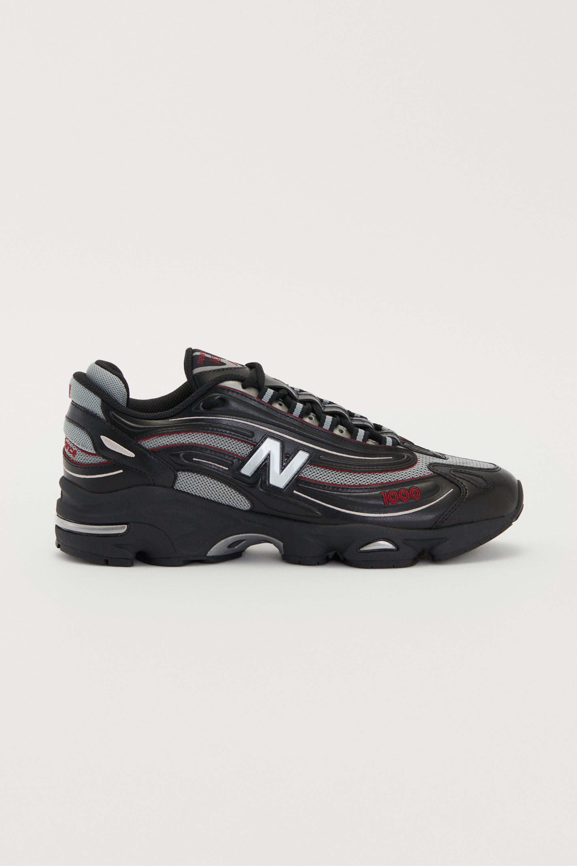 Scarpe sportive nere e grigie con un design testurizzato e accenti riflettenti. Presenta un prominente logo "N" argento di lato.