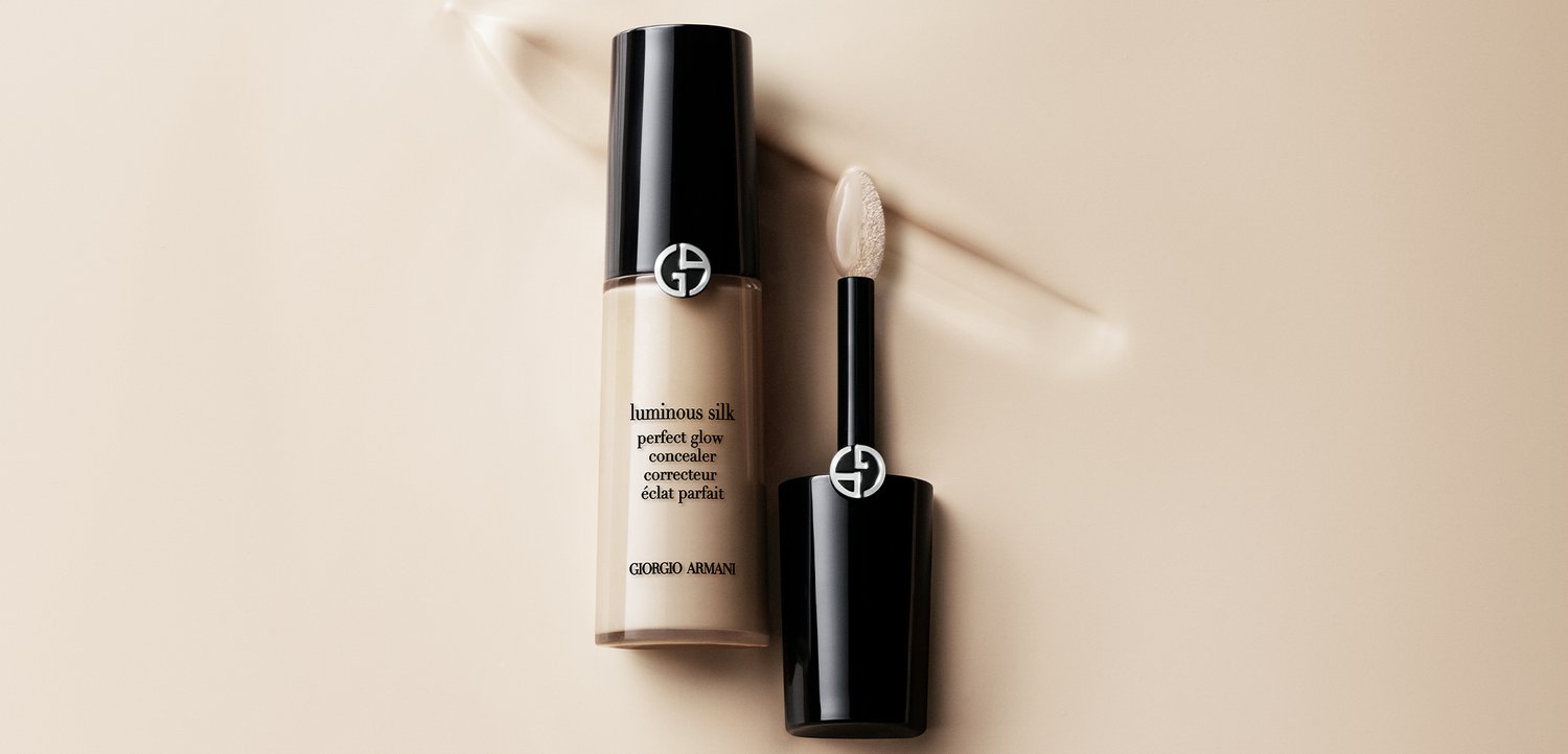 Luminous Silk Perfect Glow Concealer-Flasche und Applikator mit sichtbarer beiger Concealer-Struktur auf hellem Hintergrund.