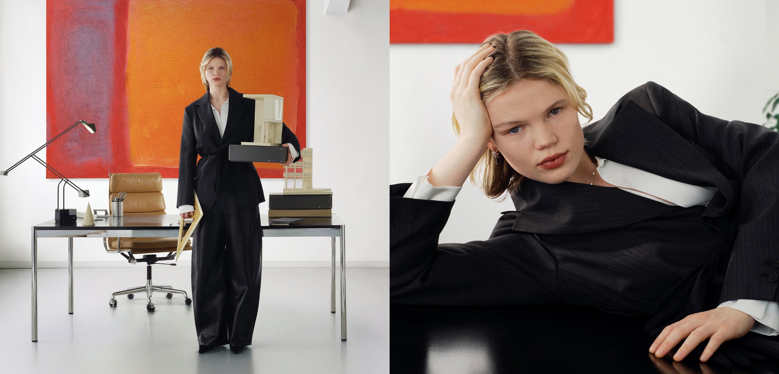 Kvinde i sort jakkesæt holder arkitekturmodel ved skrivebord med orange kunstværk, hvorefter hun læner sig tilbage på sort overflade og kigger fremad.