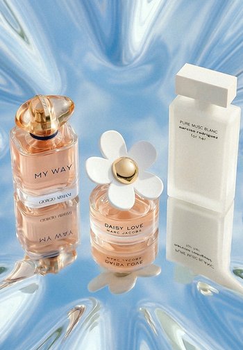 Three perfume bottles on reflective surface: Giorgio Armani My Way, Marc Jacobs Daisy Love with white flower cap, and Narciso Rodriguez Pure Musc Blanc.
