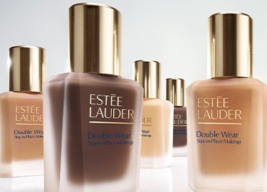 Cinq flacons de maquillage Estée Lauder Double Wear Stay-in-Place avec des bouchons dorés, présentés sur une surface blanche réfléchissante.