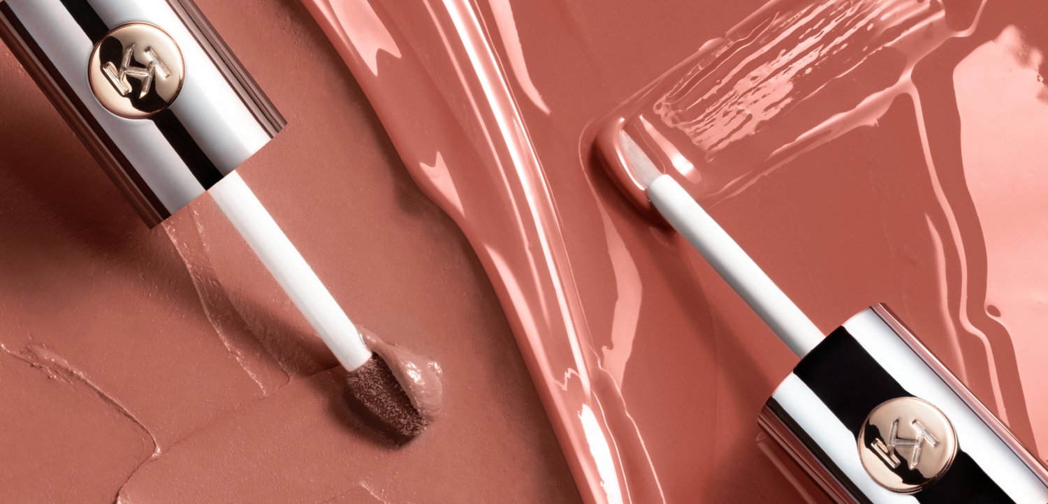 Dos aplicadores de brillo de labios rosa nude brillantes sobre un fondo de brillo de labios a juego untado.