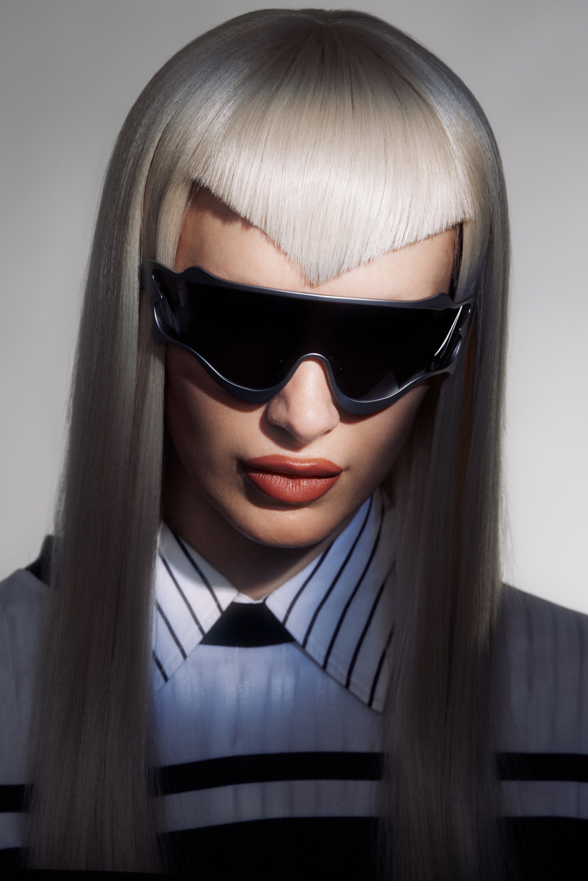 Modelo con largo cabello platino y flequillo recto lleva gafas de sol negras elegantes y una camiseta a rayas, emanando una estética moderna y fashionable.