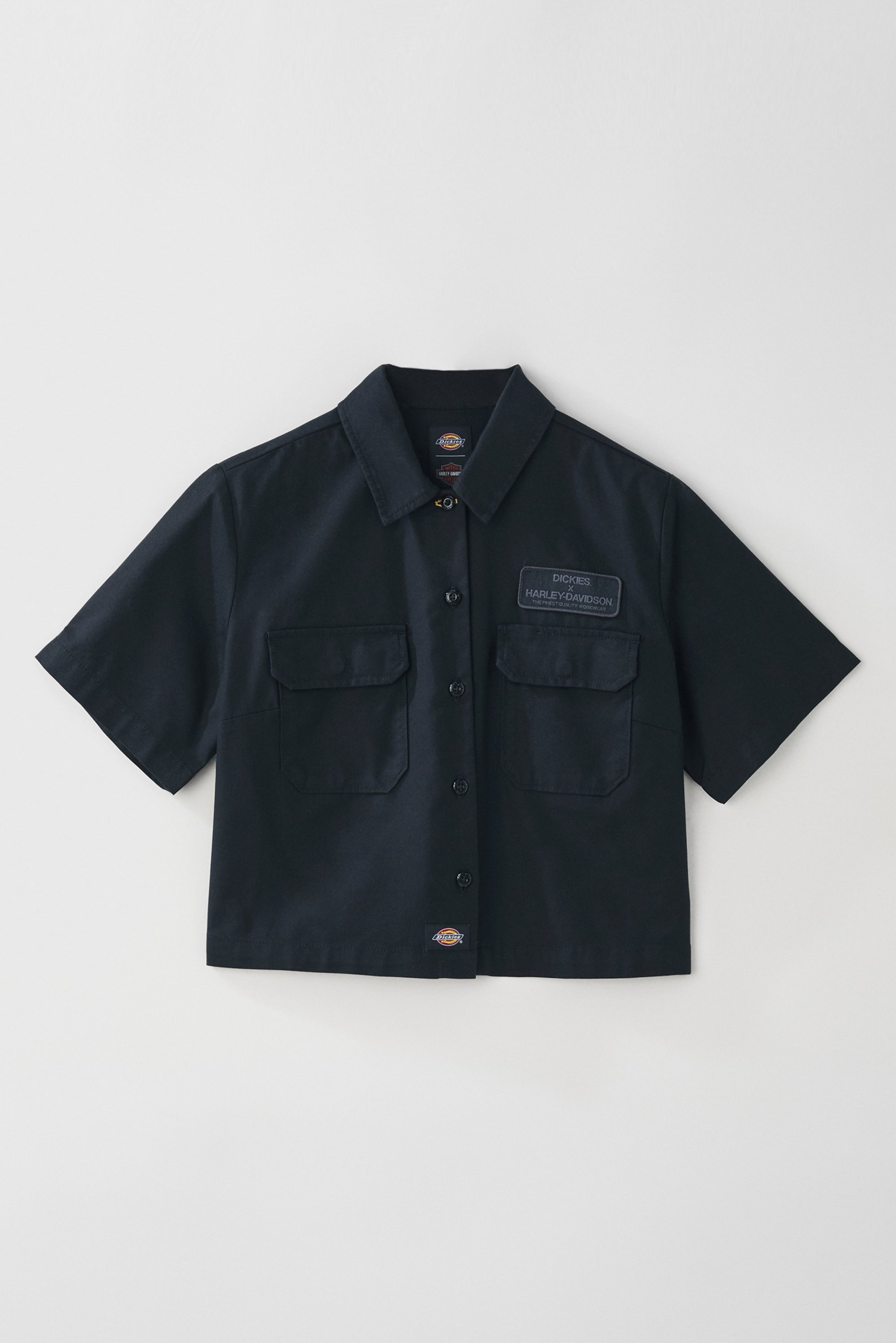 Korte mouw zwarte werkshirt met twee voorzakken en een logo patch, hangend tegen een witte achtergrond.
