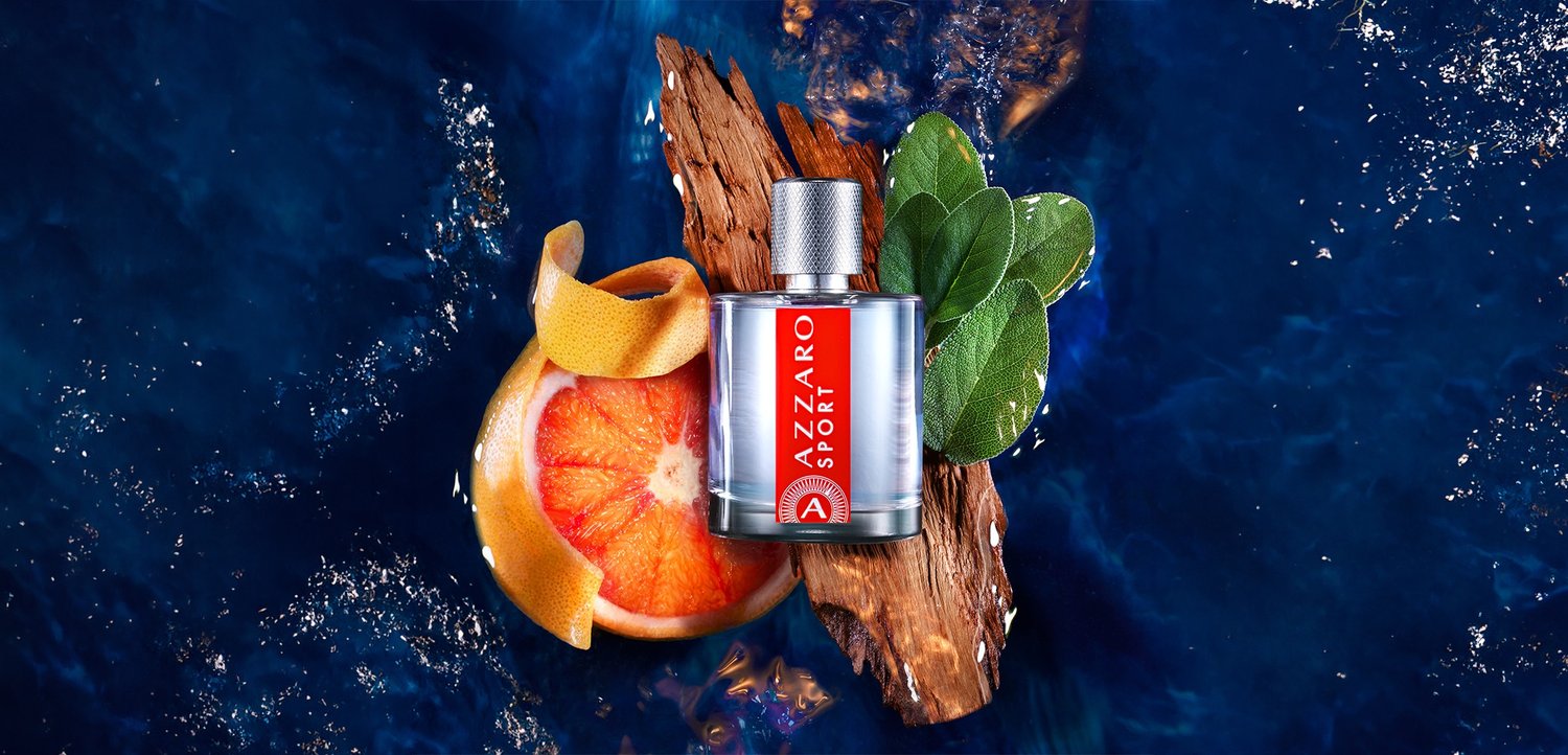 Azzaro Sport perfume bottle on wood with citrus peel, green leaves, and dark blue water background.