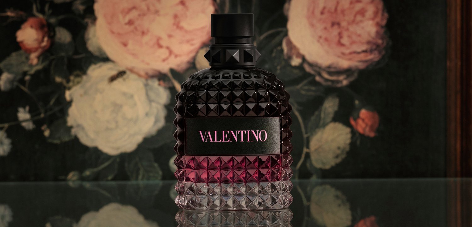 Textured glass Valentino perfume bottle with black and dark pink gradient, set against a floral painted background.