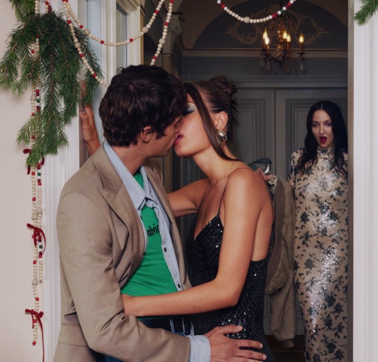 Par i en dörröppning, klädda i en ljus kavaj och en svart paljettklänning. Bakgrundsdekorationen inkluderar grönska och pärlgirlander.