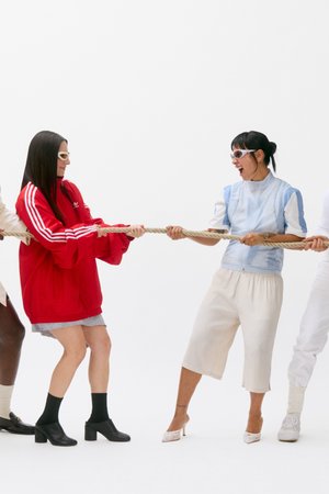 Four people take part in a tug-of-war, laughing and smiling. They are dressed in a variety of stylish outfits featuring bold colours set against a plain white background.