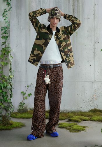 Καμουφλάζ μπουφάν, λευκό πουκάμισο, παντελόνι με λεοπάρ σχέδιο, μπλε παπούτσια και σκουφί με σχέδιο. Μπρελόκ με ένα μικρό αρκουδάκι κρέμεται από τη ζώνη.