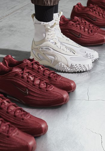 Vita höga sneakers med texturerad yta och spikad sula bredvid tre par mörkröda snörskor med stickade ovandelar.
