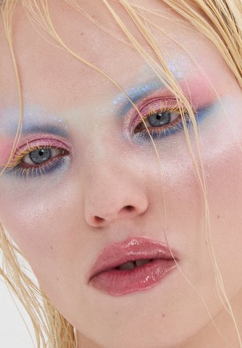 Zbliżenie na twarz z pastelowym cieniowaniem oczu w odcieniach niebieskiego, różowego i z dodatkiem połysku; błyszczące nude usta; mokre włosy z blond pasemkami.