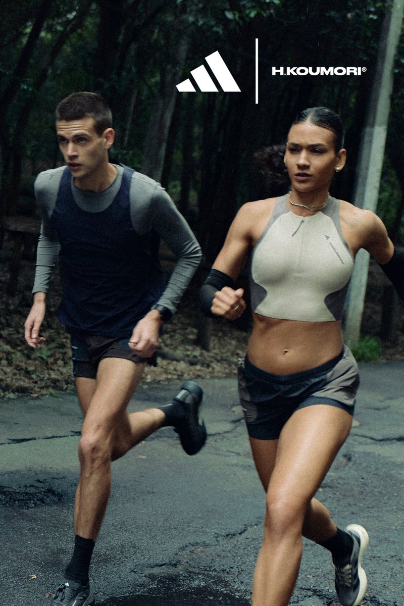 Un hombre y una mujer corren por un sendero del bosque vistiendo ropa deportiva, con los logotipos de Adidas y H.Koumori sobre ellos.