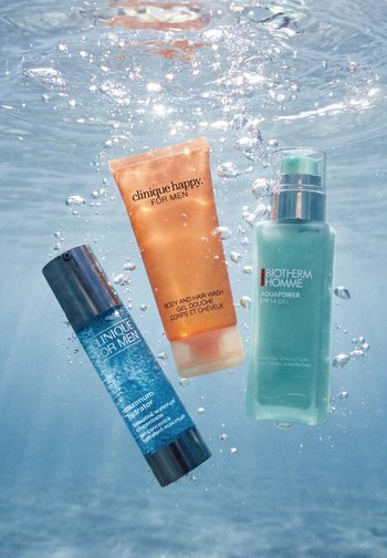 Tre prodotti per la cura della pelle maschile, inclusi Clinique Happy body and hair wash, Clinique Maximum Hydrator e il gel Biotherm Aquapower, immersi in acqua.