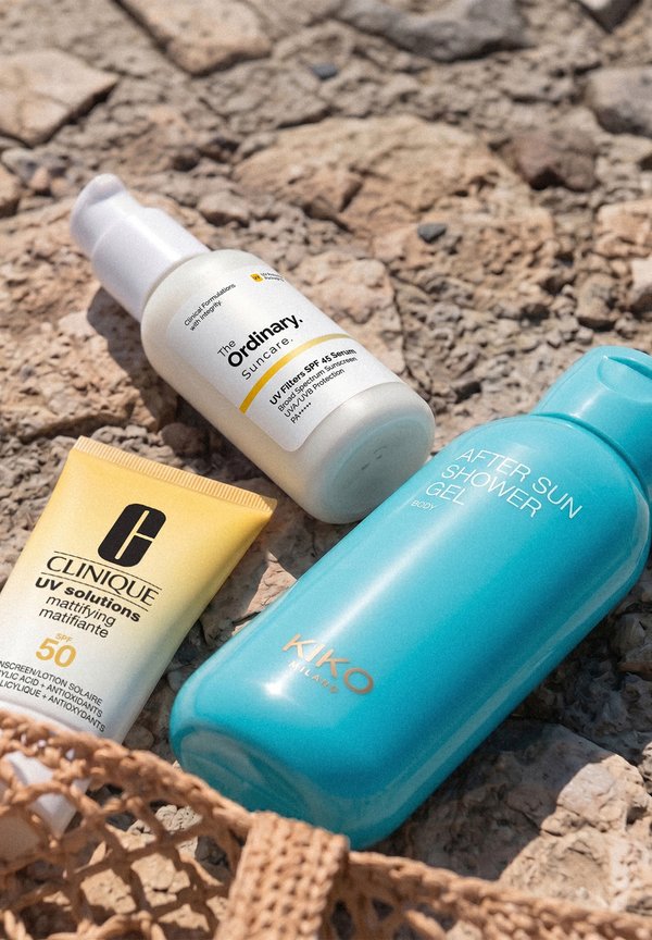 Clinique SPF 50 mattierender Creme, The Ordinary SPF 45 Serum und KIKO Milano blauer After-Sun-Duschgel auf felsiger Oberfläche.