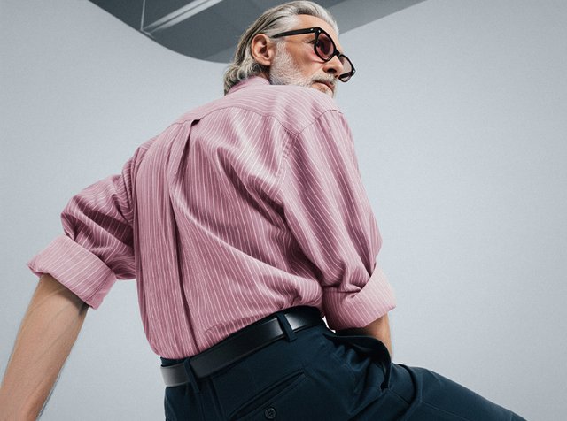 Ljusrosa randig skjorta med uppvikta ärmar, matchad med mörka byxor. Tyget verkar mjukt och slätt, utan synliga mönster eller logotyper.