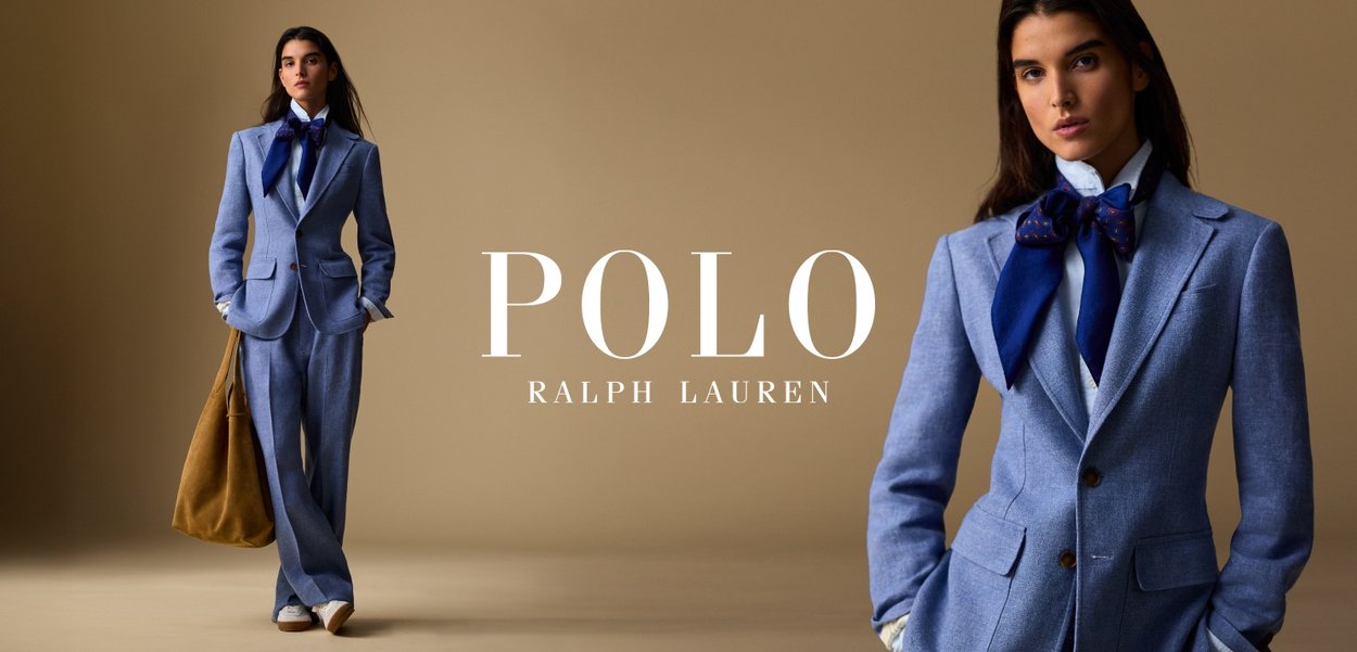 Woman in blue suit and white shirt with navy bow scarf, holding large brown bag, standing against beige background with Polo Ralph Lauren logo.