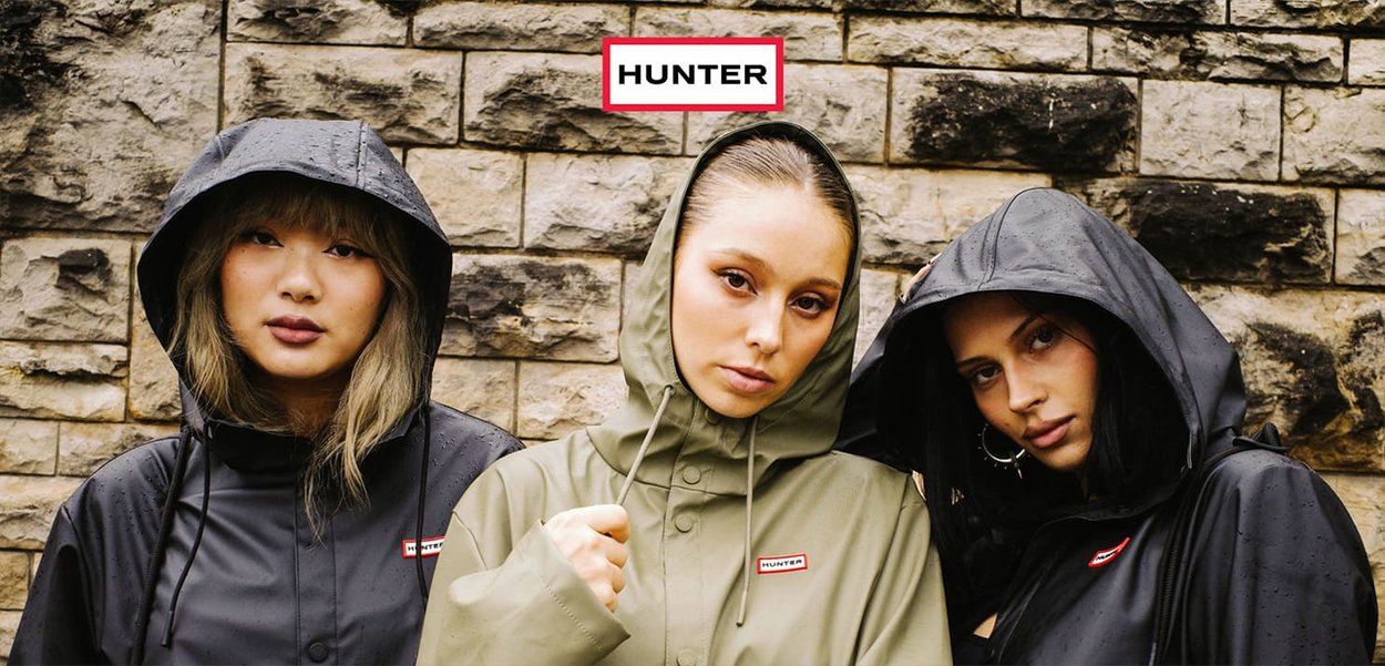 Three models wear waterproof jackets in black and olive green with hoods. The jackets feature the "HUNTER" logo in red on a white background.