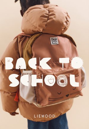 Kind met een bruine pufferjack en een bijpassende rugzak met kattengezicht ontwerp, met de rug naar de kijker, op een beige achtergrond met de tekst "Terug naar School".
