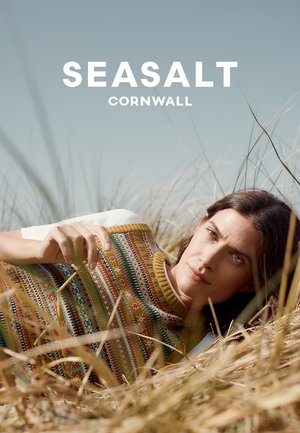 Knit sweater with multicolored patterns in earth tones. Soft texture, crew neckline, and ribbed hem against a natural backdrop of grass.