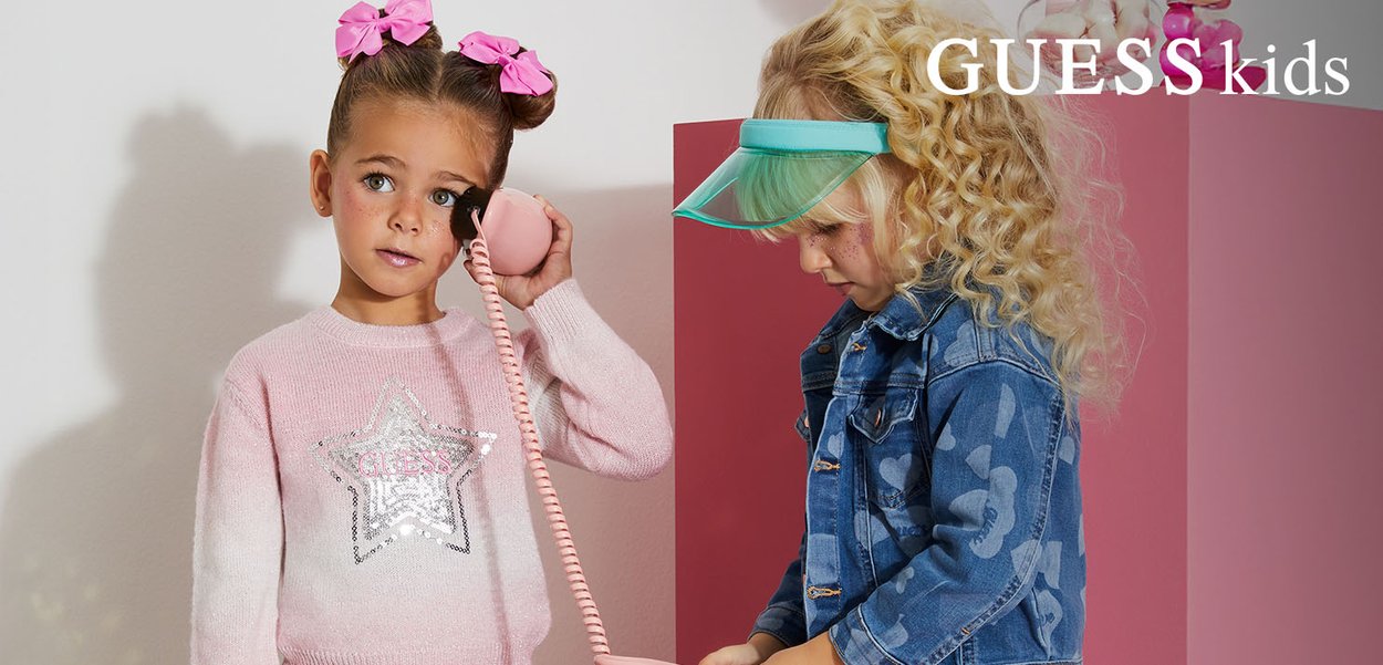 Two young girls play with a pink toy phone; one wears a pink sequin star sweater, the other a blue denim jacket and green visor.