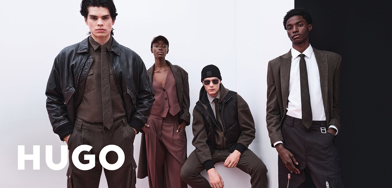 Four models wearing brown and black structured outfits, standing and sitting against a white and black background with "HUGO" text visible.