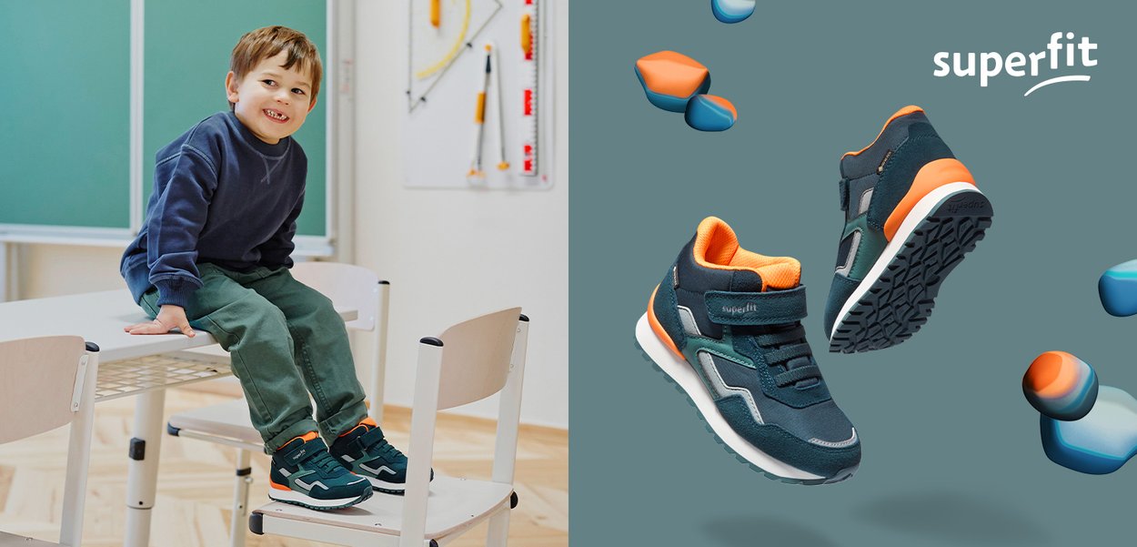 Smiling boy sitting on classroom table wearing dark blue and orange sneakers with Velcro straps, next to floating shoe pair on teal background.