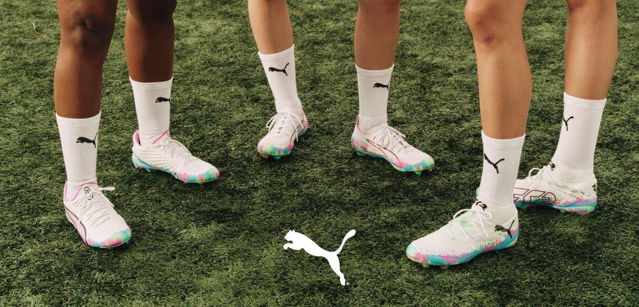 Puma soccer cleats in white with a colorful gradient sole. Players wear white socks with the Puma logo, standing on green turf.