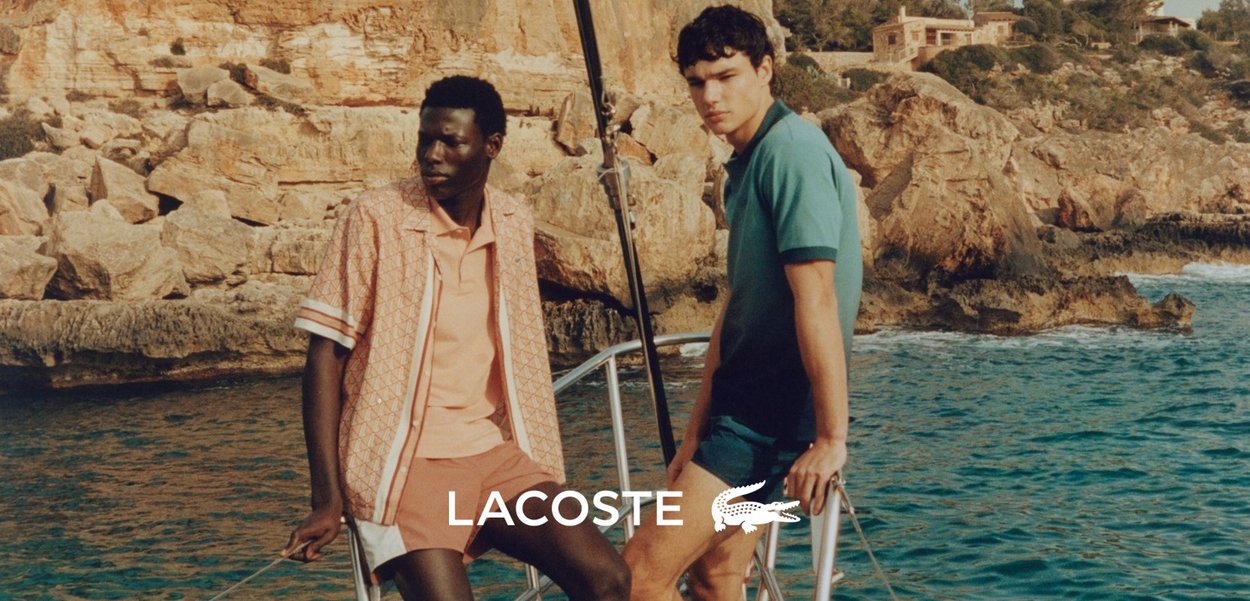 Due uomini su una barca vicino a scogliere rocciose. Uno indossa una camicia e pantaloni corti a fantasia rosa; l'altro indossa una camicia e pantaloni corti di un verde teal uniforme.