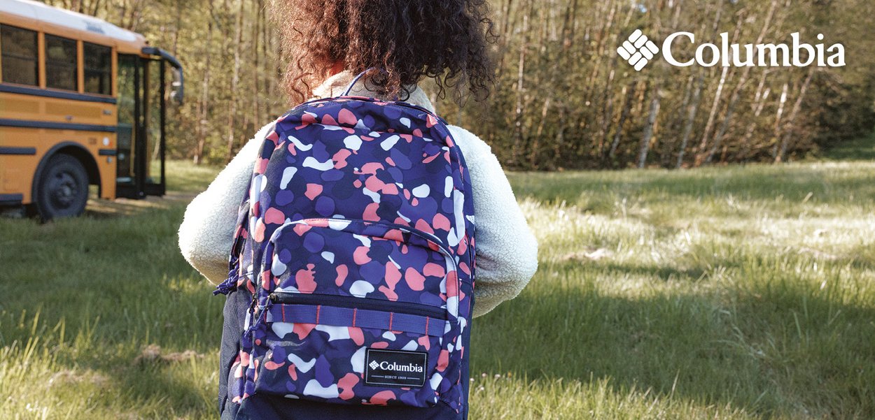 Sac à dos Columbia en bleu marine avec des formes abstraites rose et blanche, doté de bretelles ajustables et d'une poche zippée à l'avant, sur un fond de gazon.