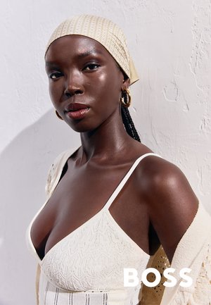 Top senza maniche color crema con motivi a maglia testurizzati, abbinato a un foulard leggermente decorato e grandi orecchini a cerchio dorati.