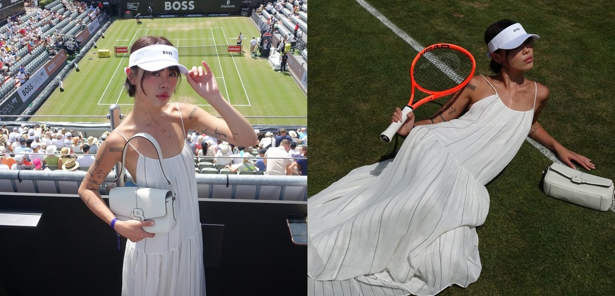 Weißes Faltenkleid, weiße Handtasche mit Hardware-Details, weißes Visier, hält einen orangefarbenen Tennisschläger auf einem Rasentennisplatz, bei hellem Tageslicht.