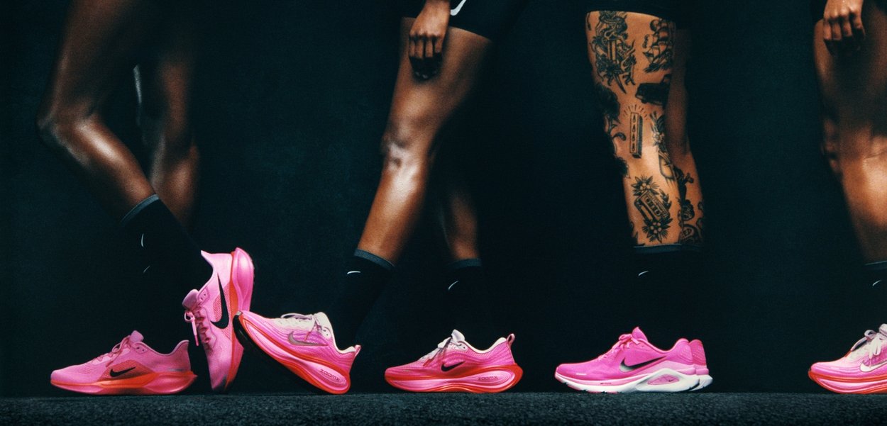 Lyserøde Nike løbesko vist på fødderne, med en åndbar mesh-overdel, polstring og teksturerede såler. Tatoveringer synlige på benene.