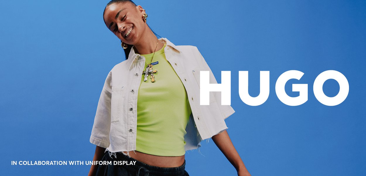 White denim short jacket over a bright green fitted top, paired with black pants. Features a pendant necklace and a blue background.