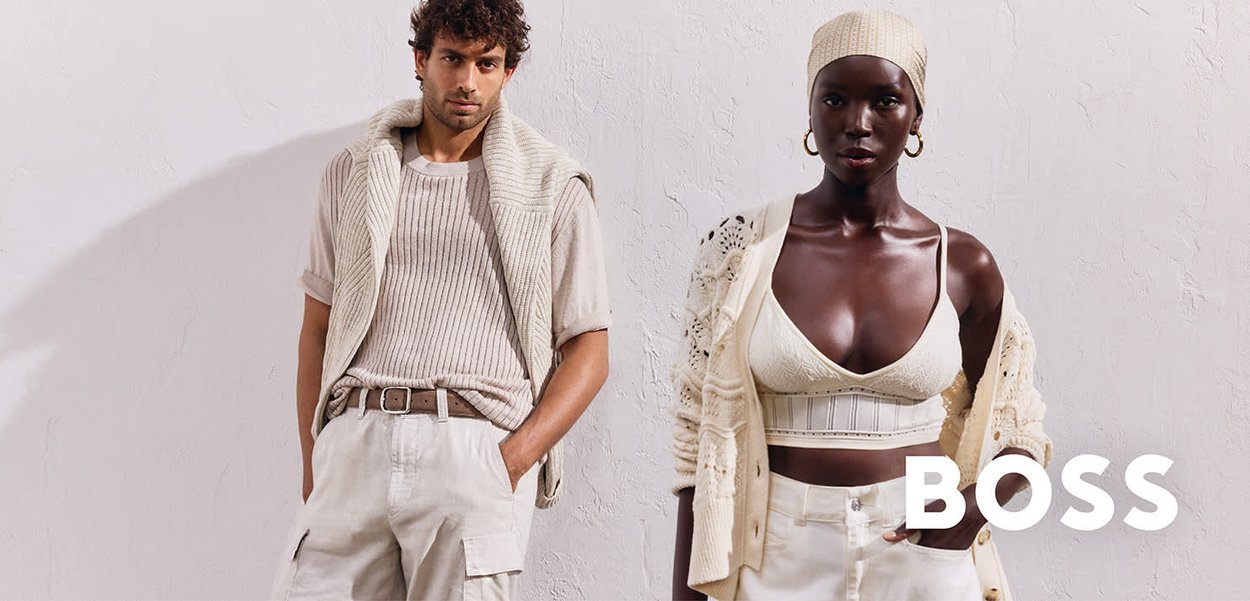 Due modelli si trovano davanti a uno sfondo bianco texturizzato. Il modello maschile indossa una maglietta beige a coste e pantaloni cargo color crema. La modella femminile indossa un cardigan leggero e intricato su un bralette coordinato e pantaloni color crema.